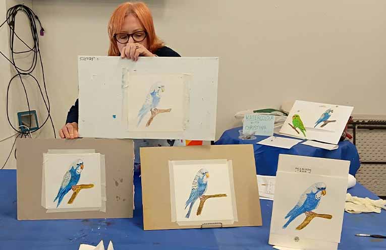 Tutor, Christina Reid, displays the class’s work on watercolour budgies.